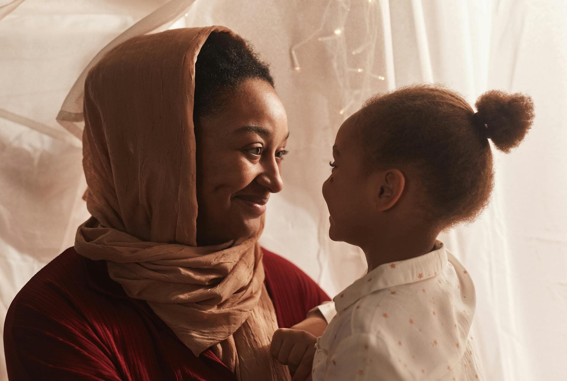 Photo by Werner Pfennig on Pexels A heartwarming moment between a mother in a hijab and her daughter indoors, sharing smiles and affection.