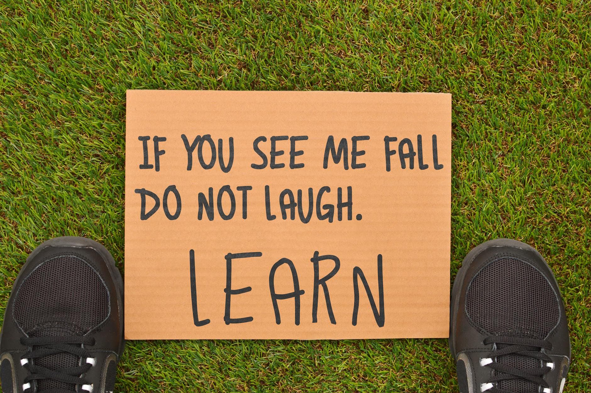 Photo by Renee B on Pexels Cardboard sign with motivational message beside sneakers on green grass.