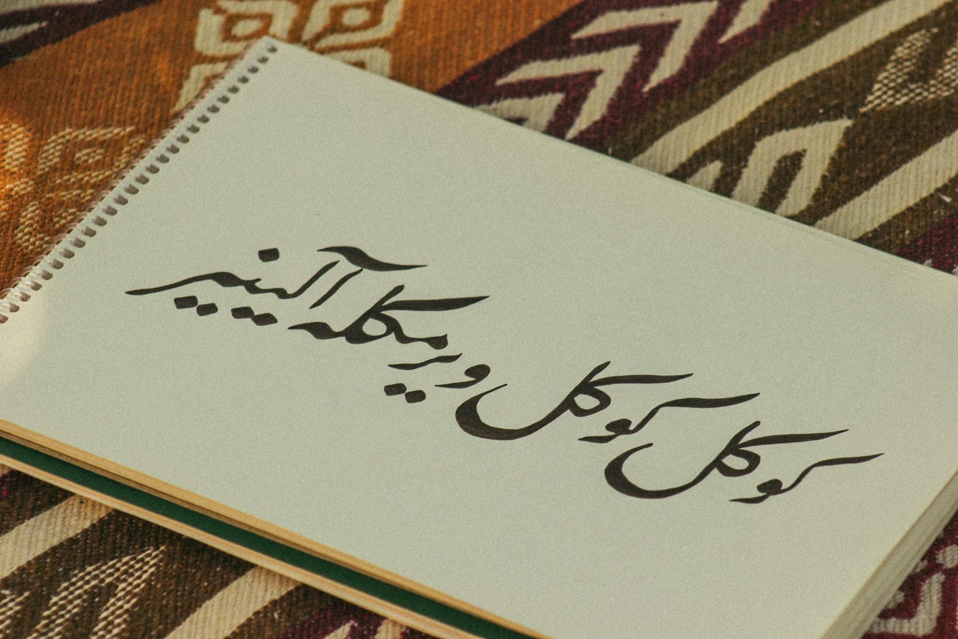 Photo by feyza ebrar on Pexels Notebook with Persian calligraphy on colorful patterned fabric background.