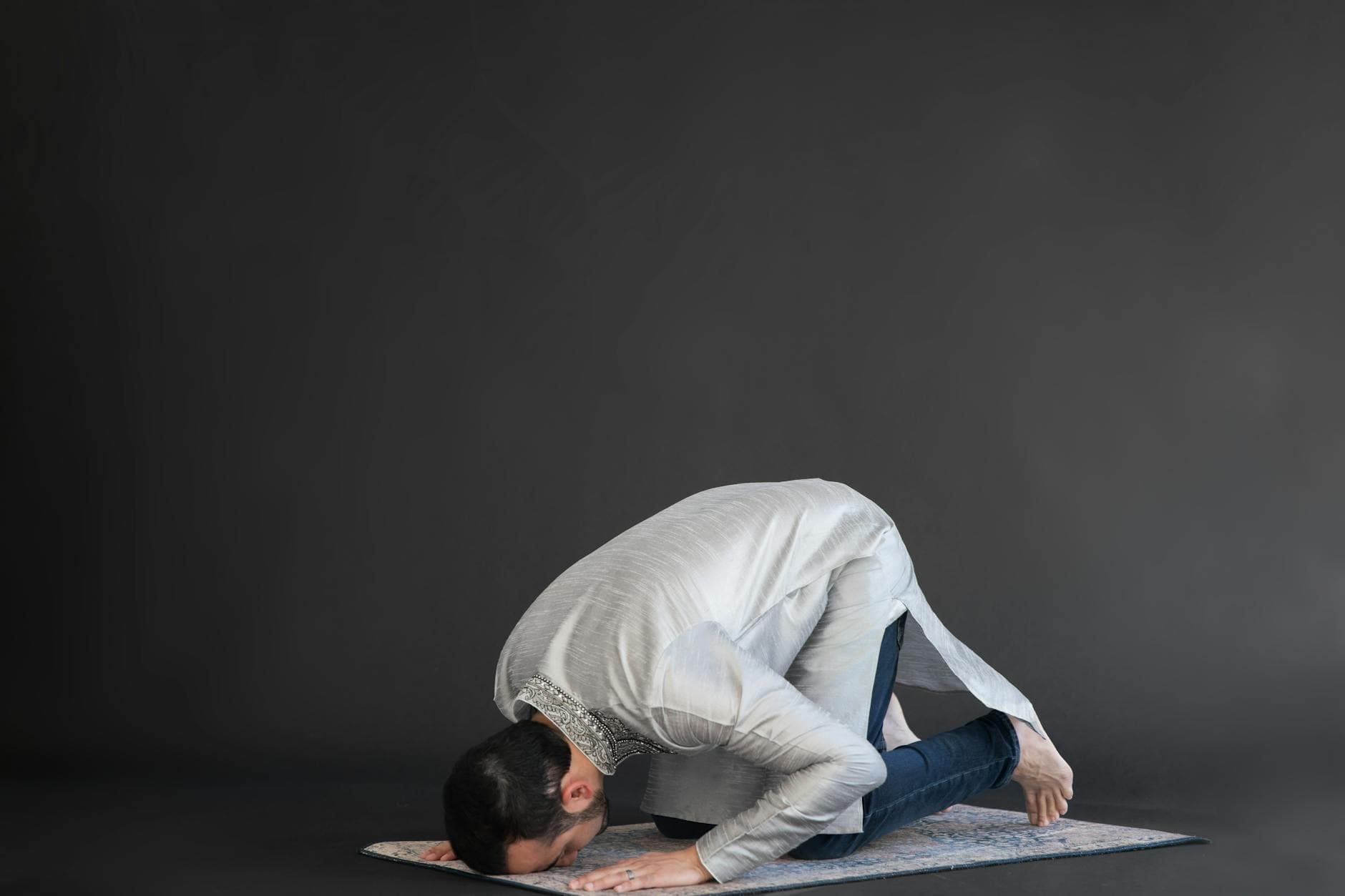 Photo by RDNE Stock project on Pexels A man dressed in traditional attire performing a religious prayer indoors on a prayer mat.