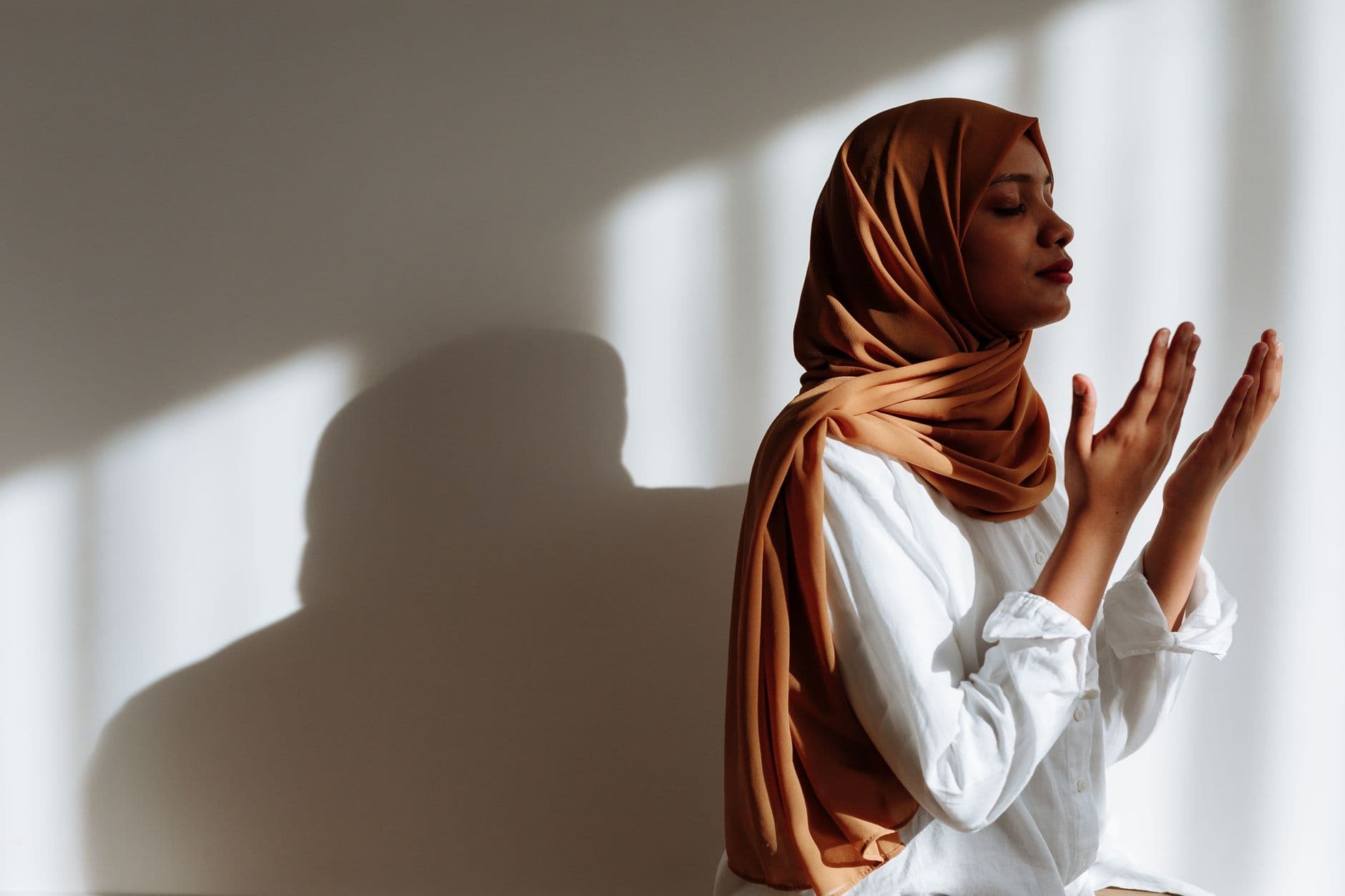 Photo by Thirdman on Pexels A woman in a hijab praying, surrounded by soft sunlight, reflecting contemplation and spirituality.