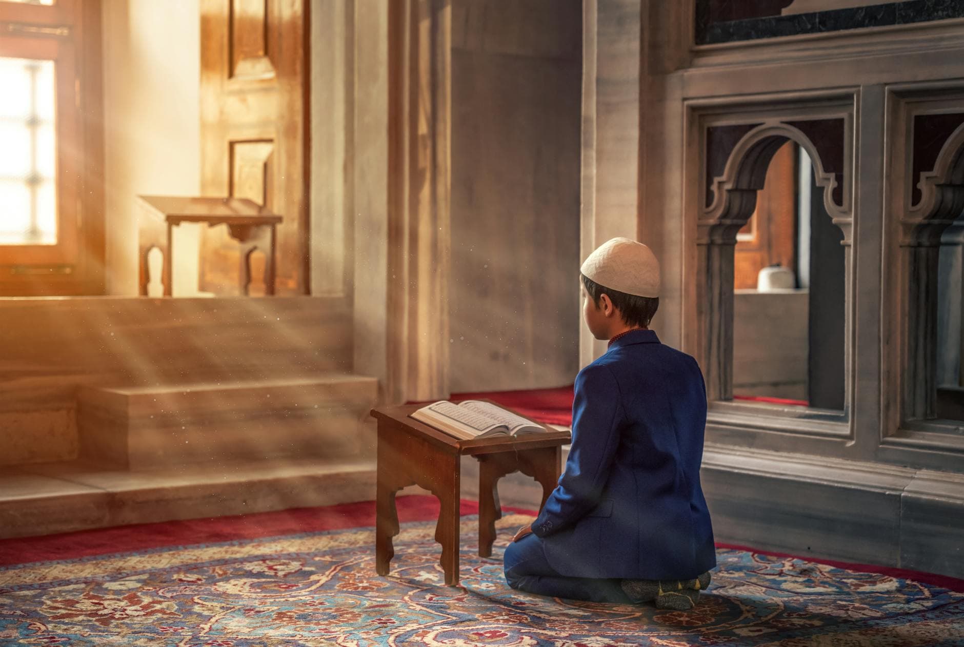 Photo by Abdullah Ghatasheh on Pexels A young boy kneels in prayer inside a mosque with sunlight streaming through the window.