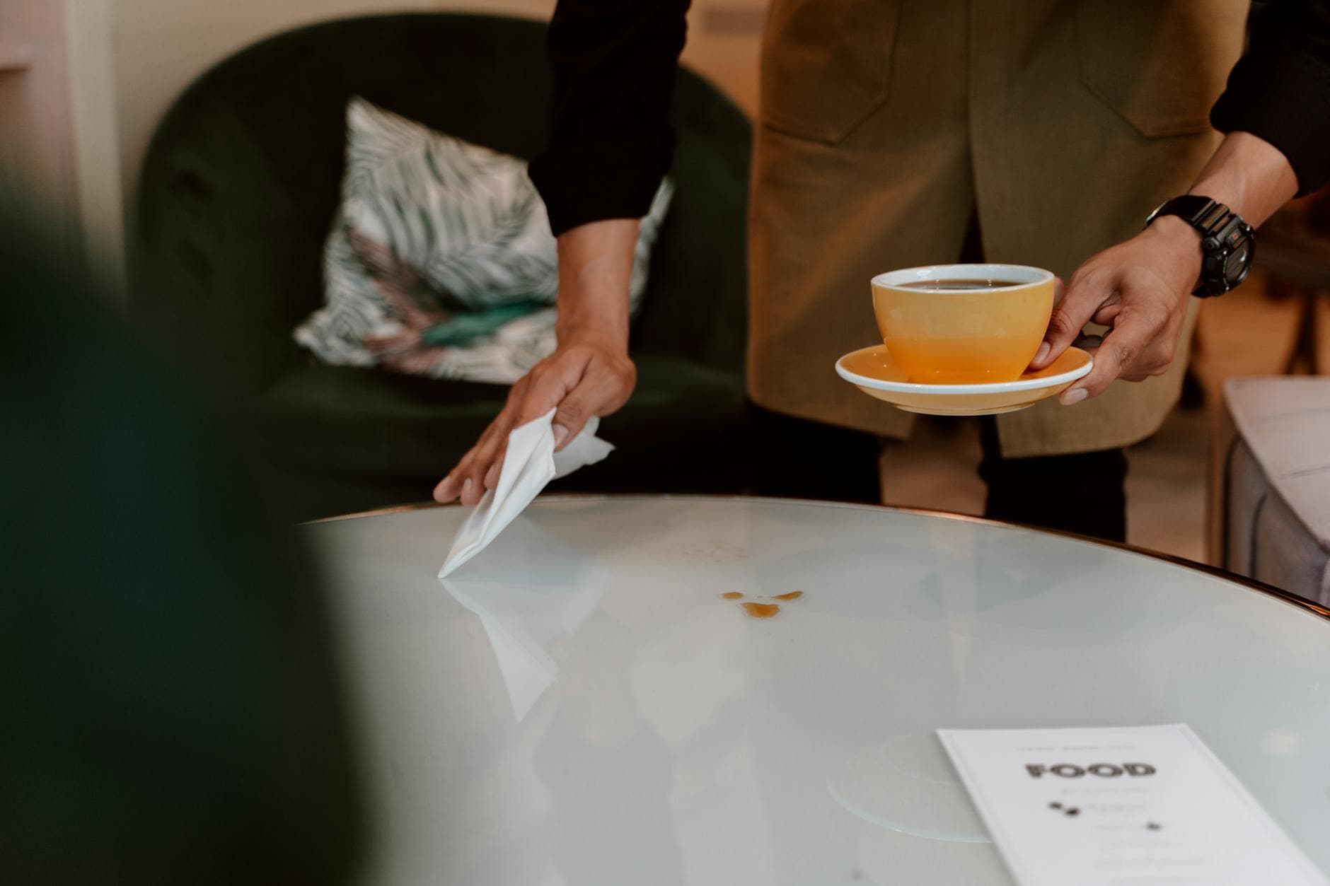 Photo by RDNE Stock project on Pexels A barista holding a coffee cup and cleaning a table in a cozy cafe setting.