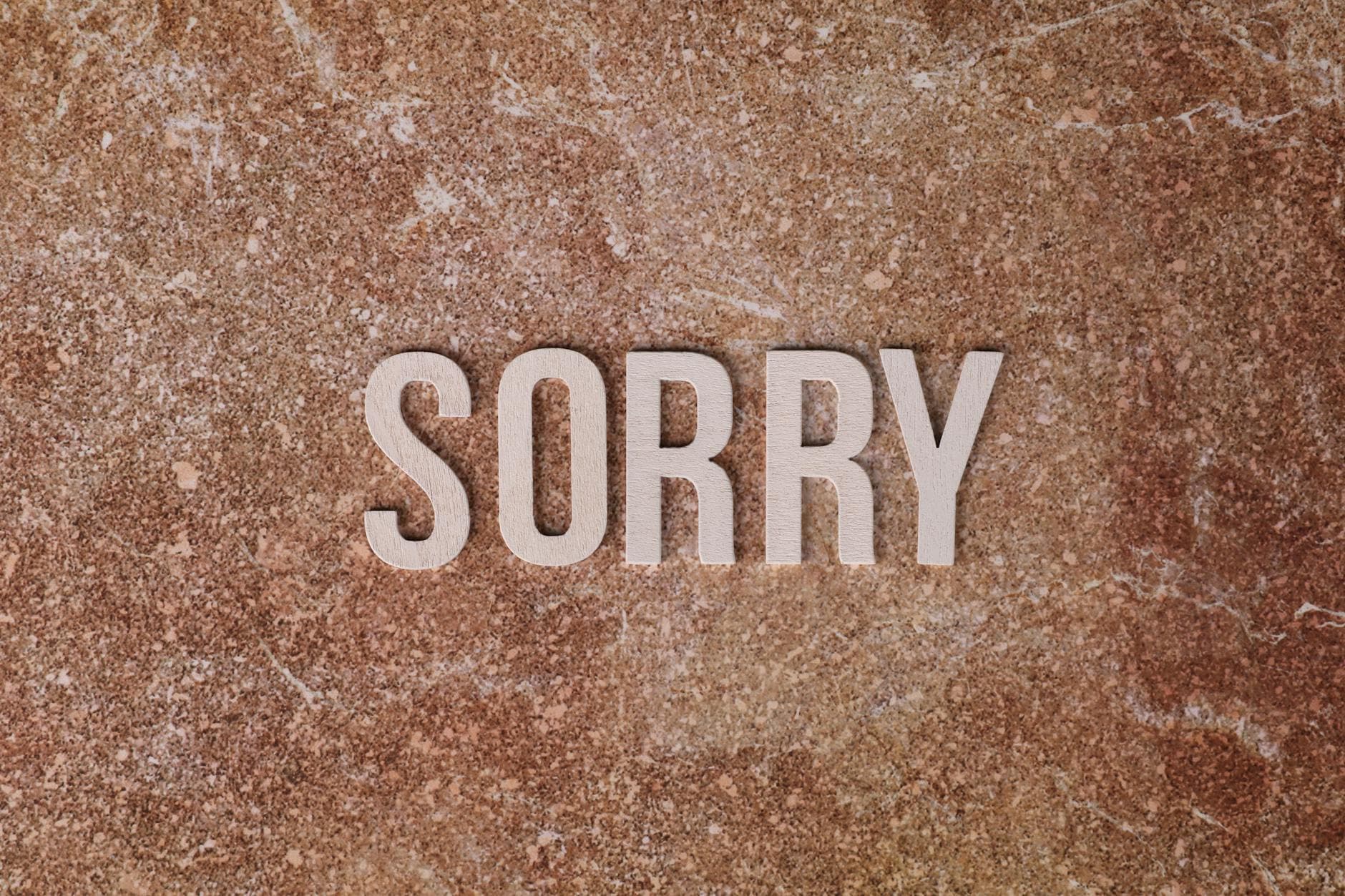 Photo by Ann H on Pexels Wooden letters spell 'SORRY' on a textured brown stone background, expressing apology.